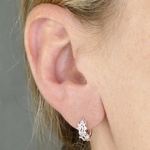 A close-up of a person's ear wearing the Barbara silver huggie hoop earring with a textured, leaf-like  pattern with sparkling cz.